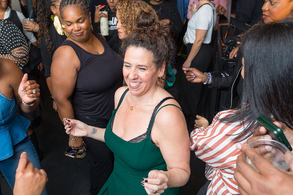 The honoree in green dancing — arms out, fully present, completely herself