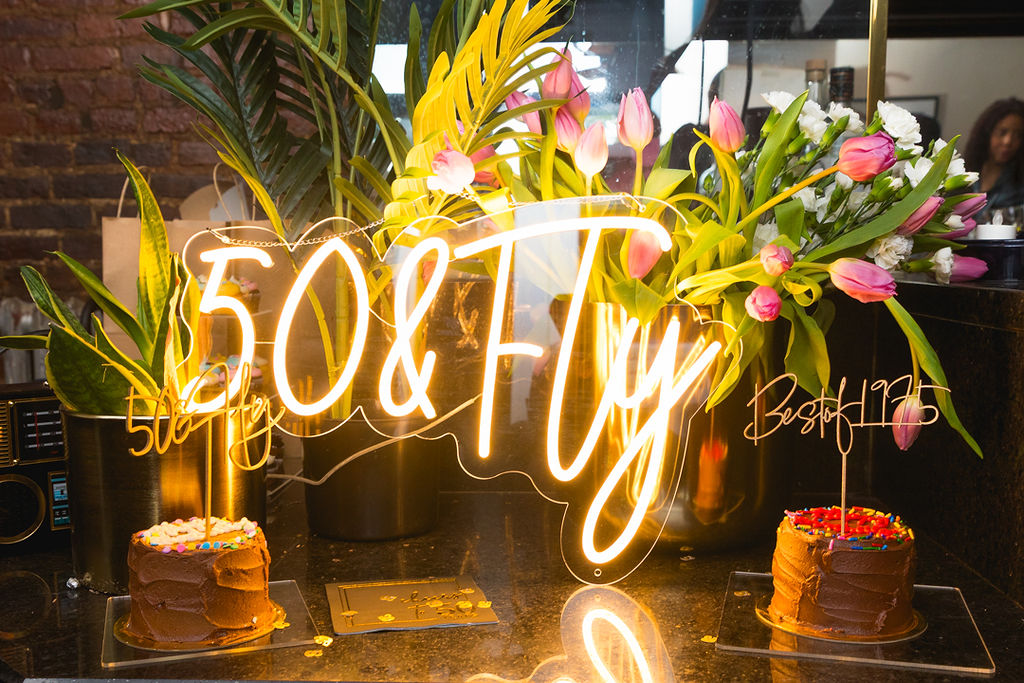 50 and Fly neon sign with birthday cakes and florals