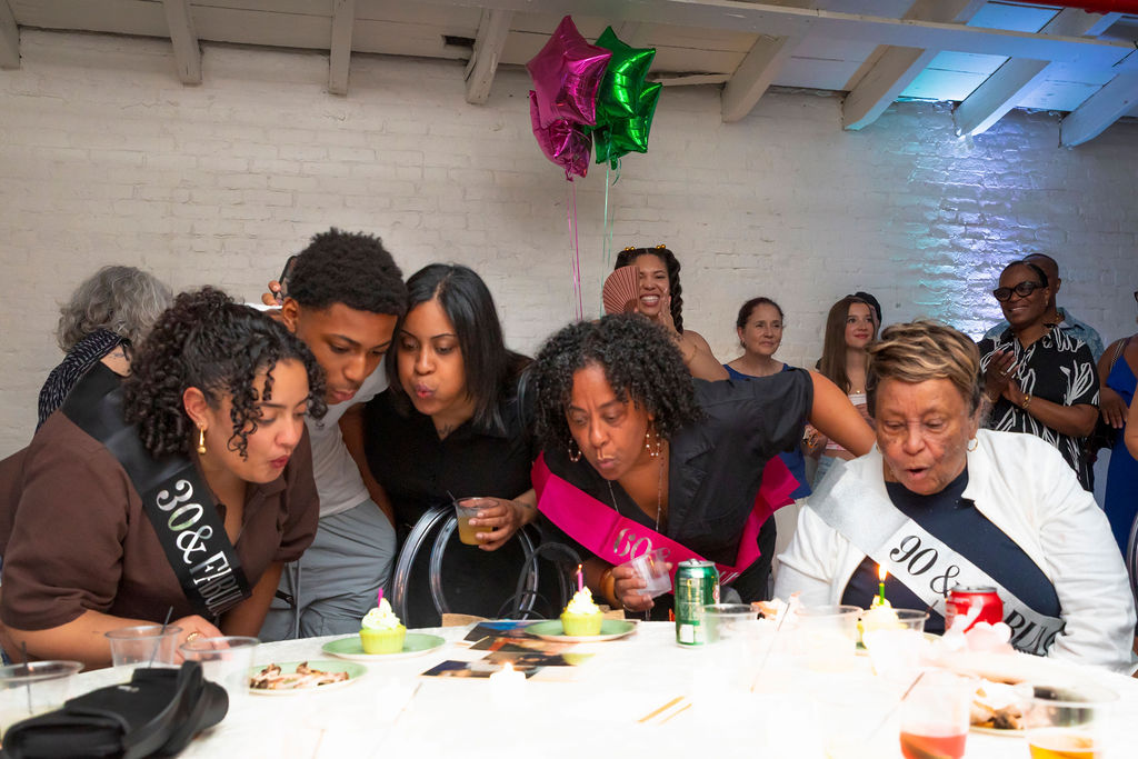 The candle moment — three women leaning in together, sashes reading 30, 60, and 90