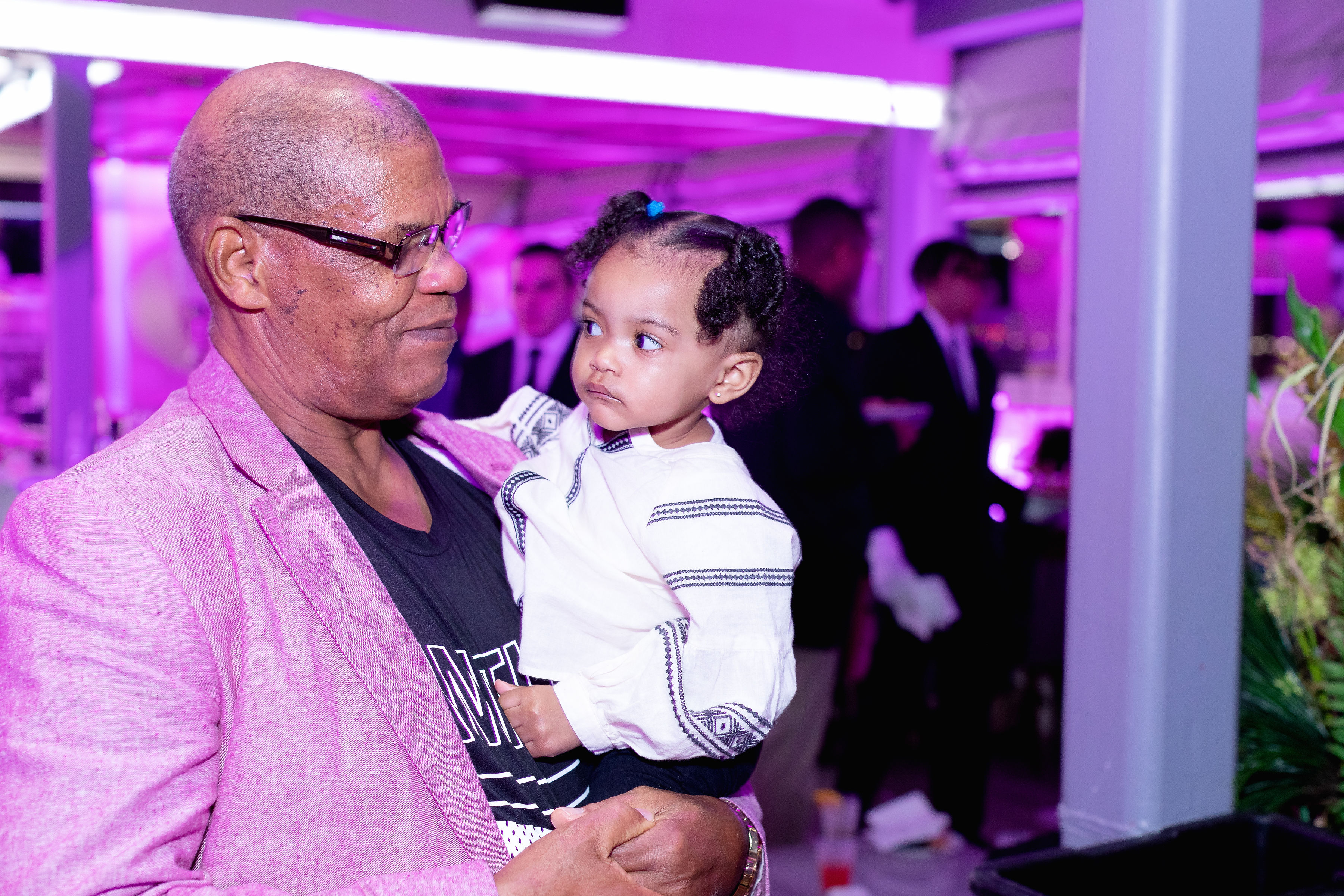 Grandfather in pink blazer holding a young girl — the youngest generation at the celebration