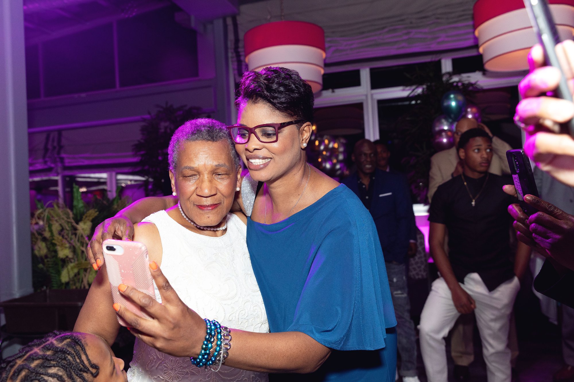 Double embrace — honoree hugged from both sides by family, full room of celebration behind