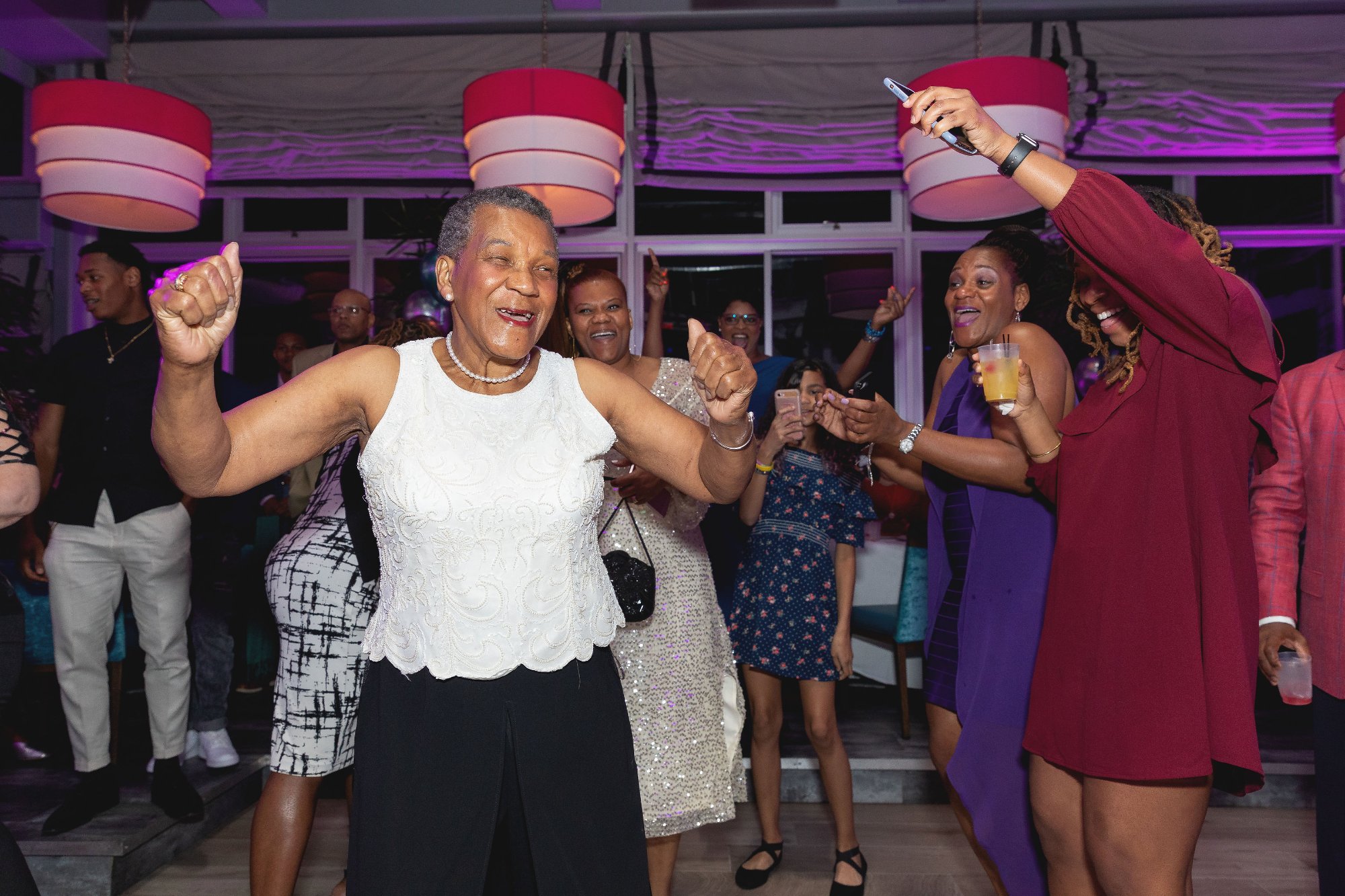 Honoree dancing with grandson — pure joy, blue dance floor light, colorful balloons behind