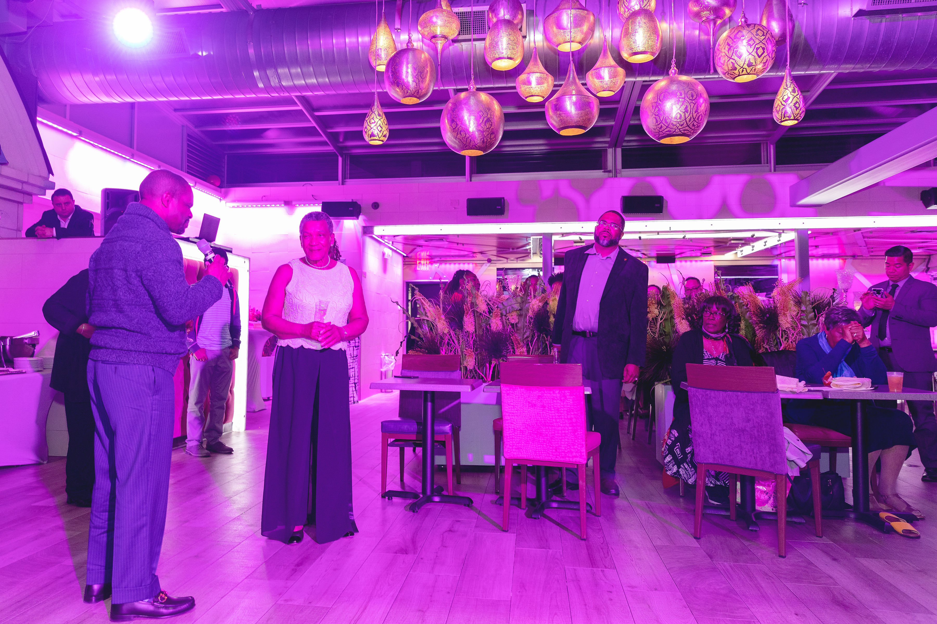The venue wide — Moroccan pendant lamps, pink uplighting, the honoree being toasted