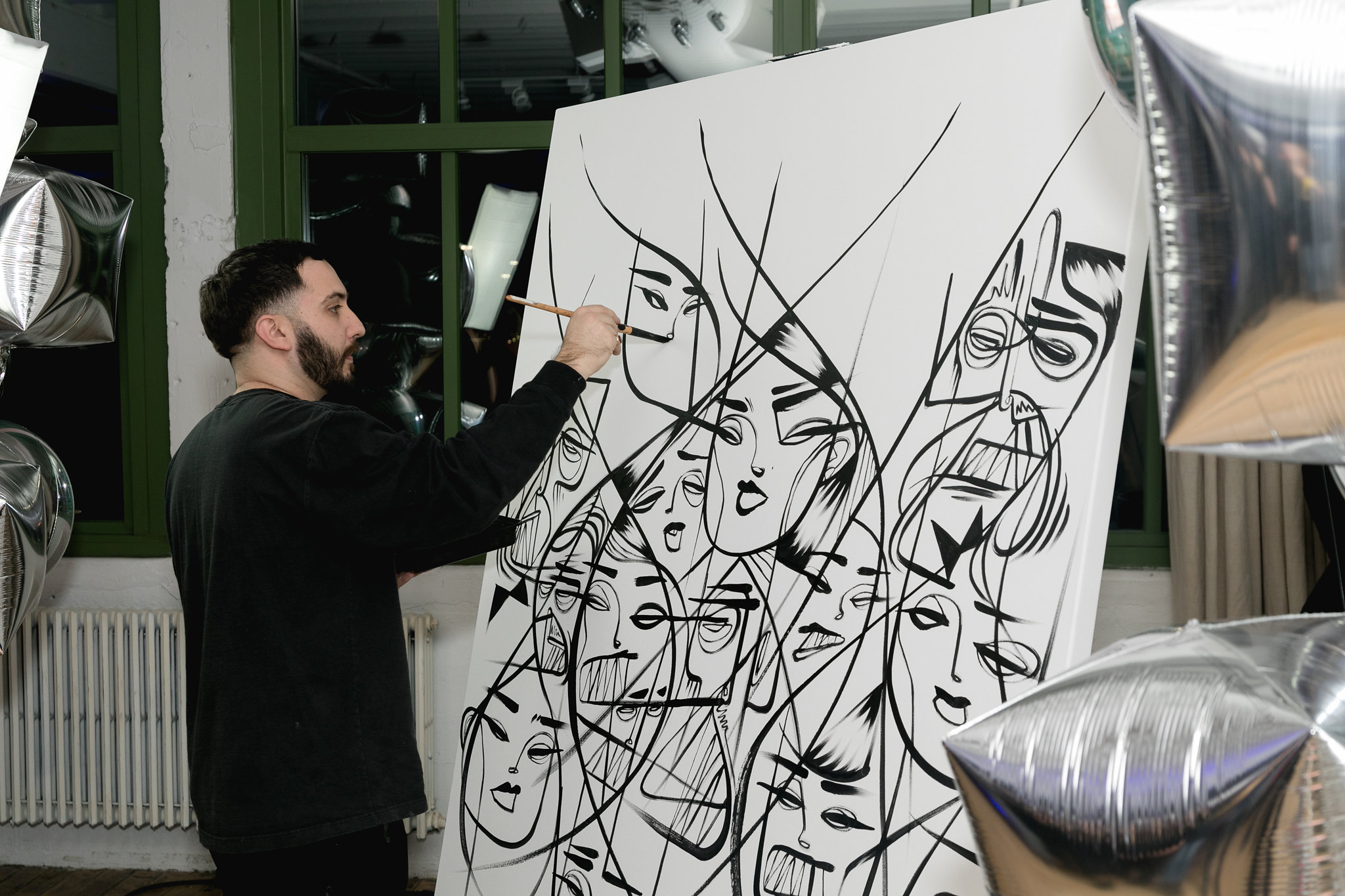 Live painter working on a large canvas mid-gala — bold ink strokes, silver balloons surrounding him