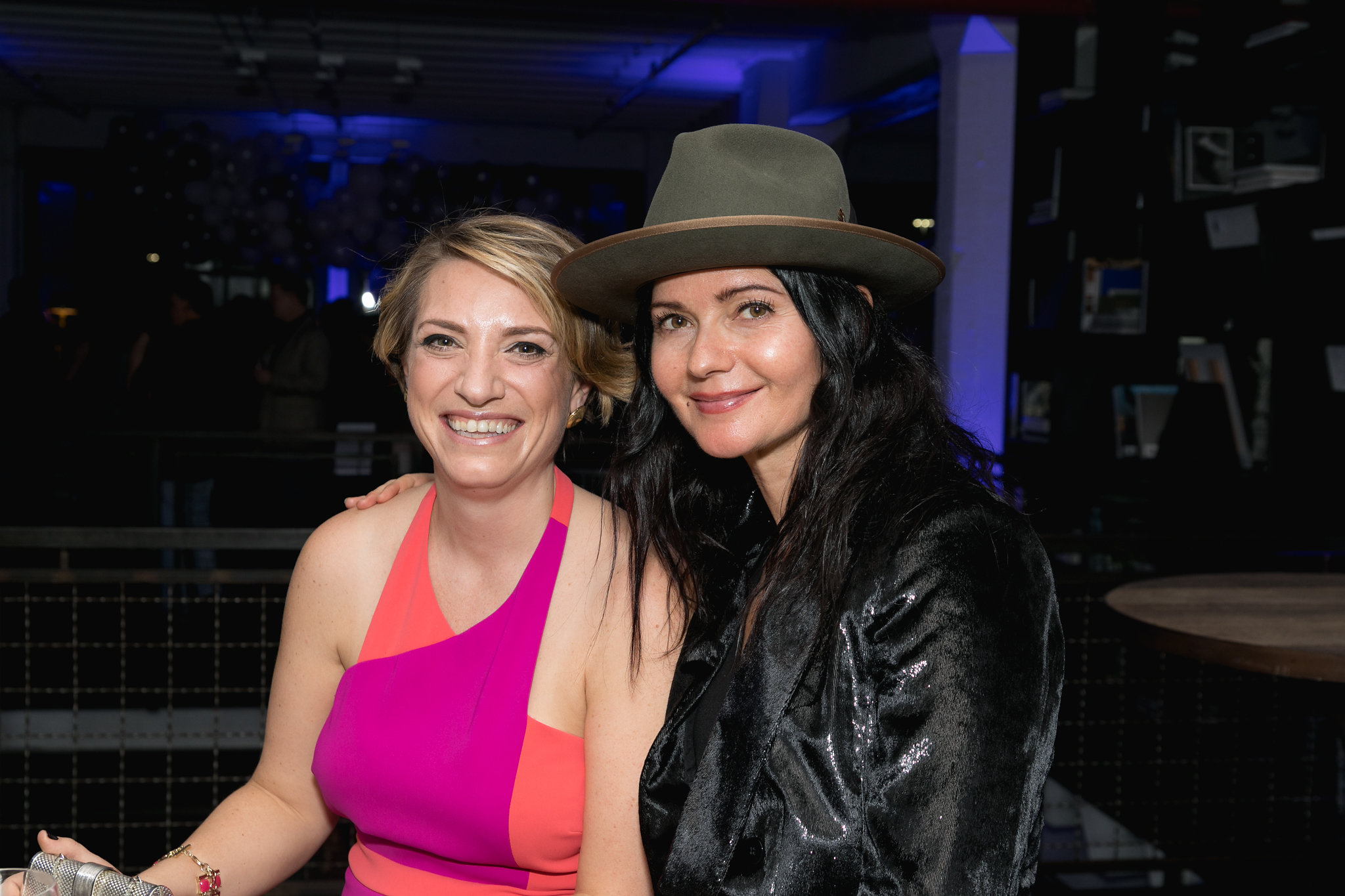 Two guests mid-evening — warmly lit, in conversation, the energy of the room around them