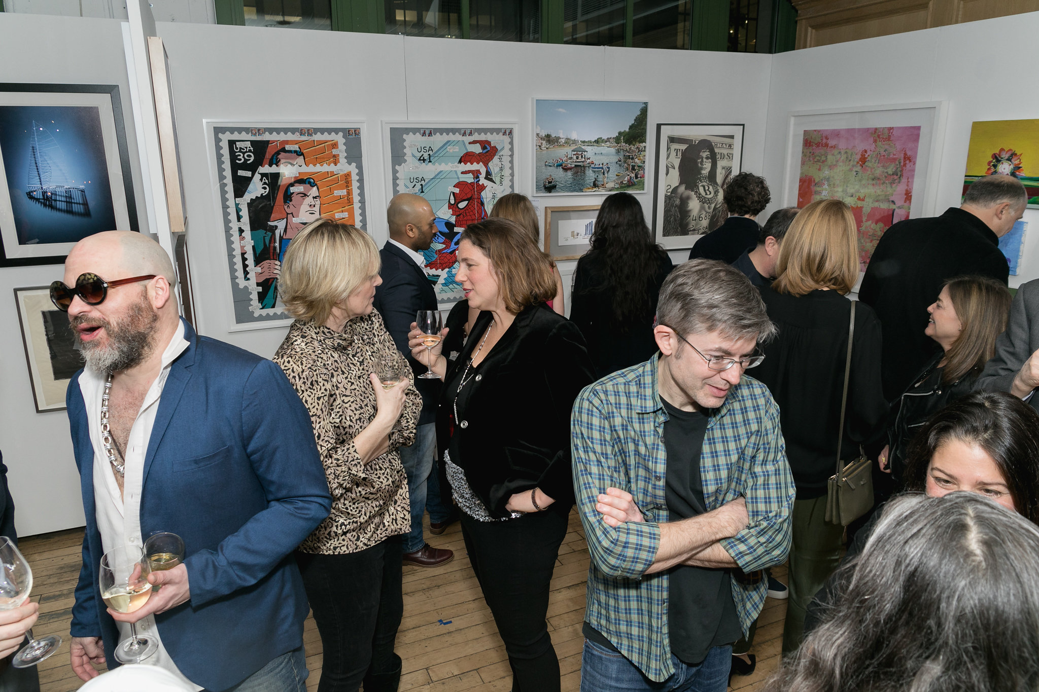 Guests moving through the gallery — animated conversation in front of large framed works