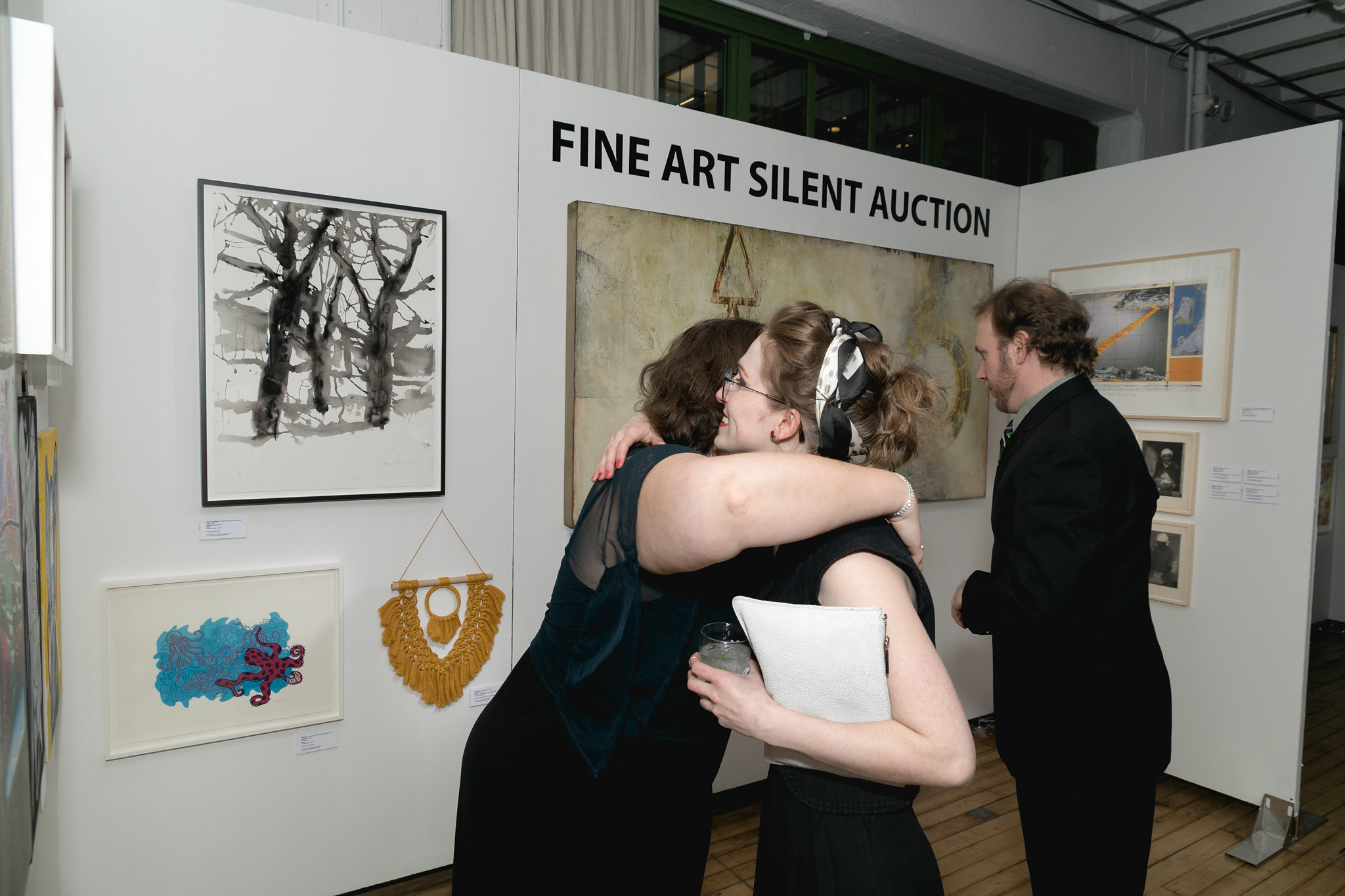 Two guests embracing in front of the Fine Art Silent Auction sign — joy and connection