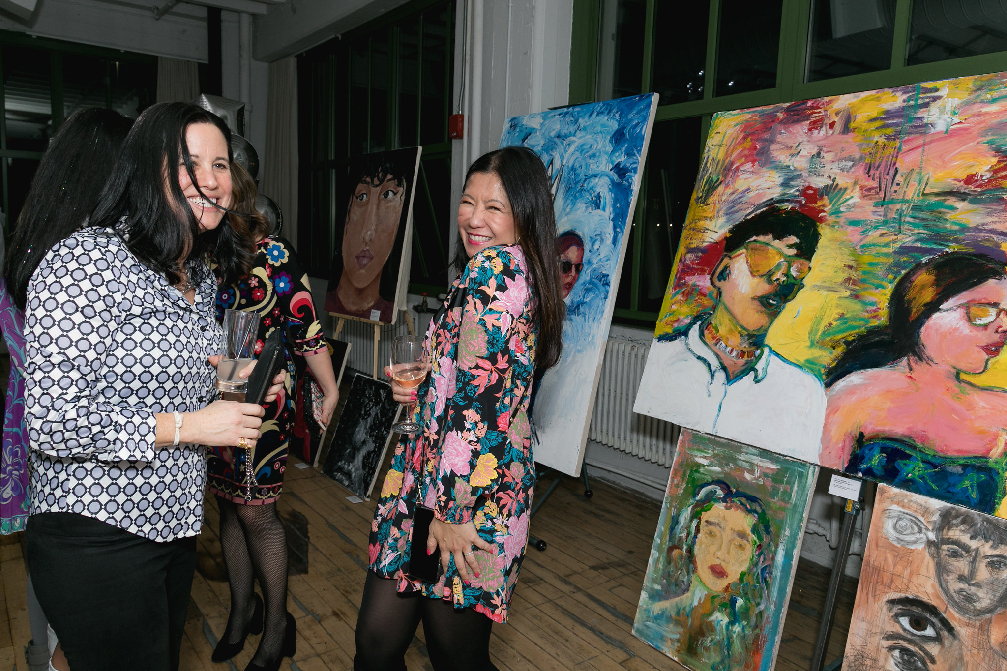 Two guests laughing in front of large colorful canvases — art as backdrop to connection