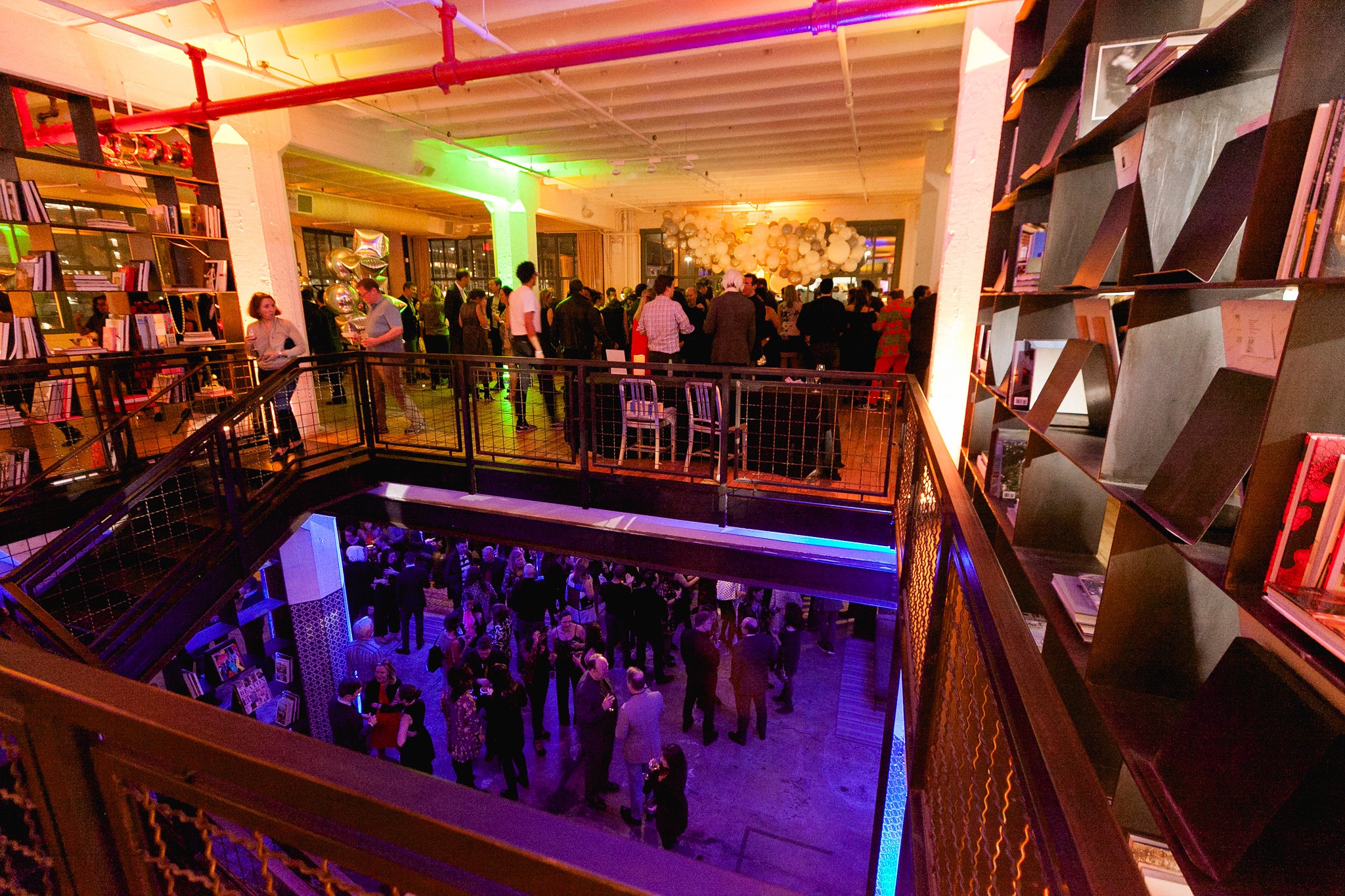 Aerial view from the mezzanine — packed room below, green and orange light, the full crowd visible