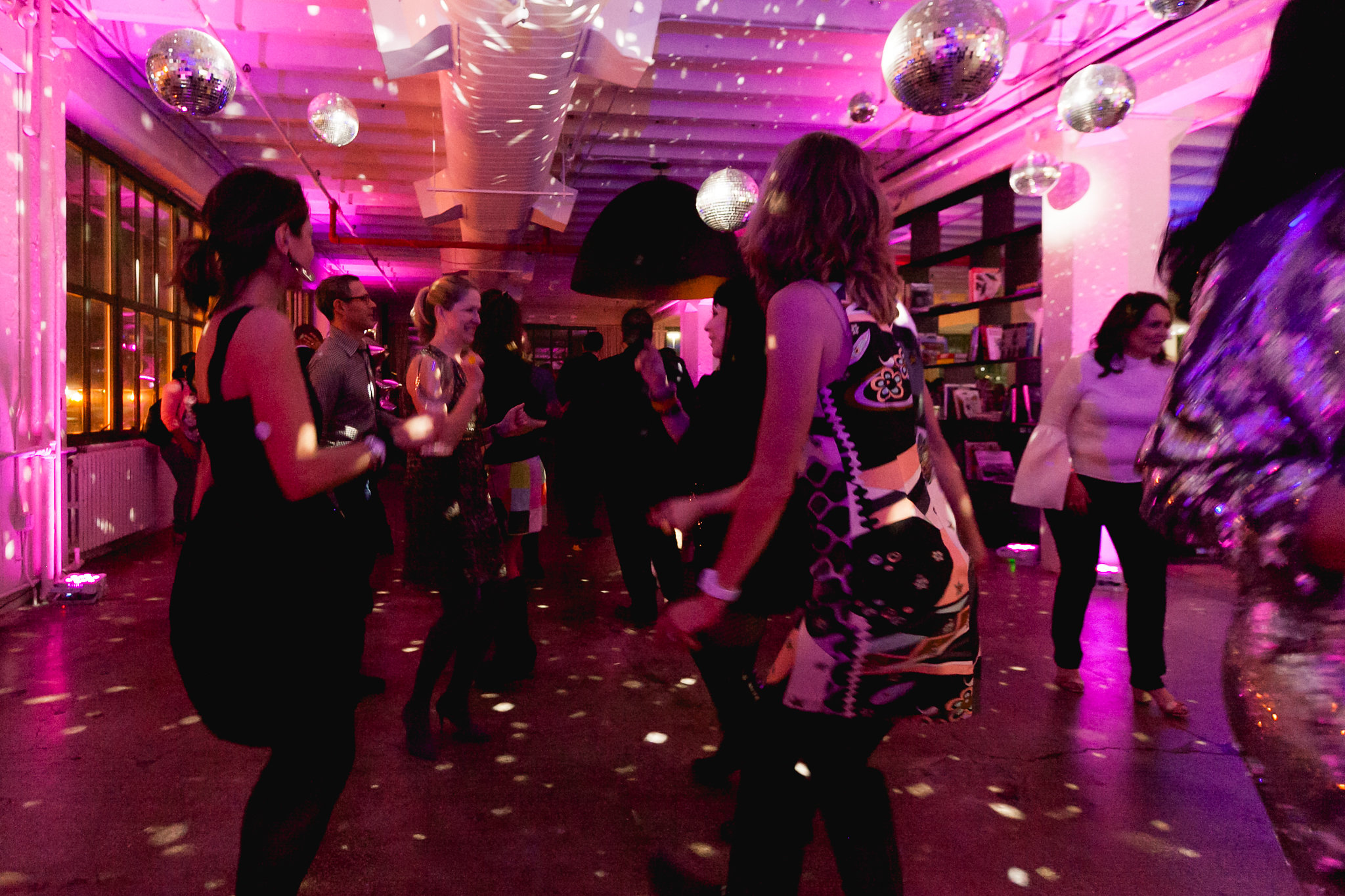 The dance floor at full energy — disco balls overhead, pink light, motion blur, the room completely alive