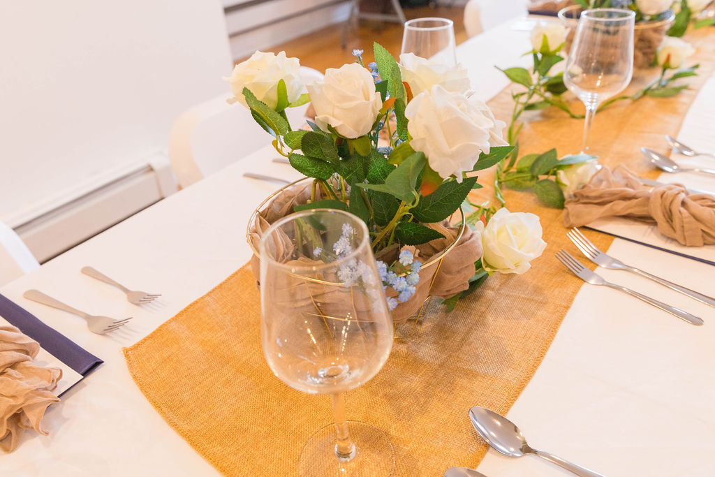 Table detail close-up — white roses, wine glass, burlap runner, place setting