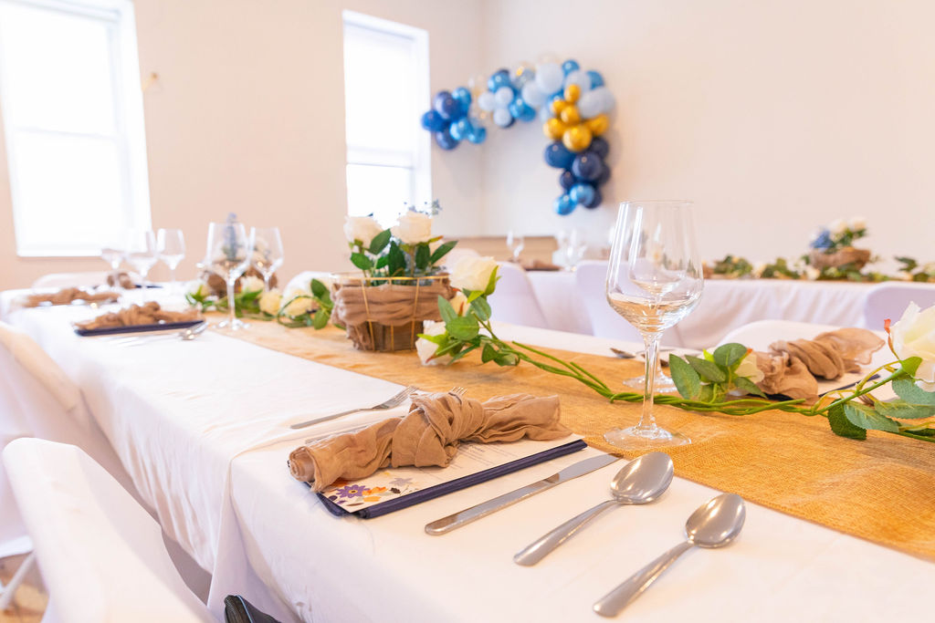 The table set and waiting — white roses, burlap runner, balloon arch in navy and gold