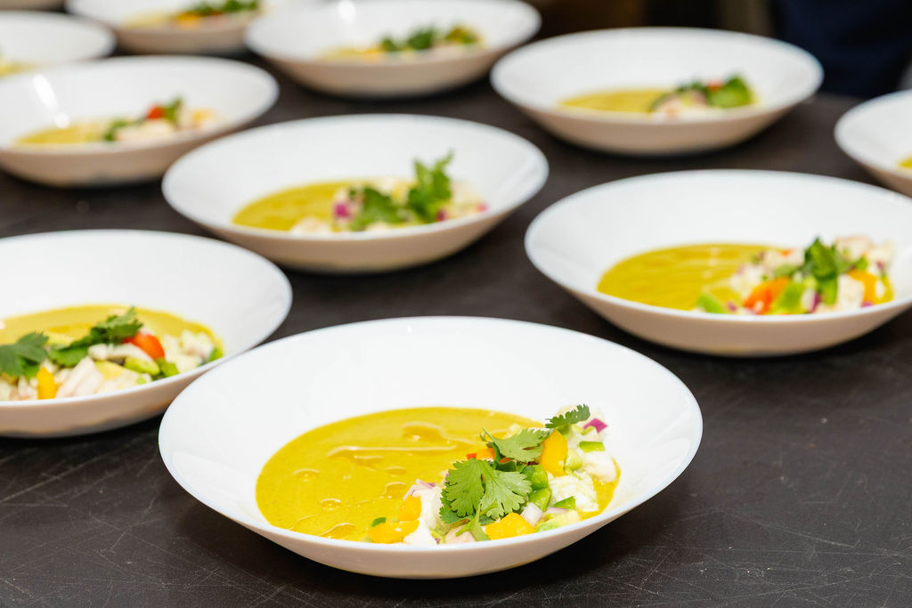 Twelve ceviche bowls plated and ready for service — golden leche de tigre, cilantro crown