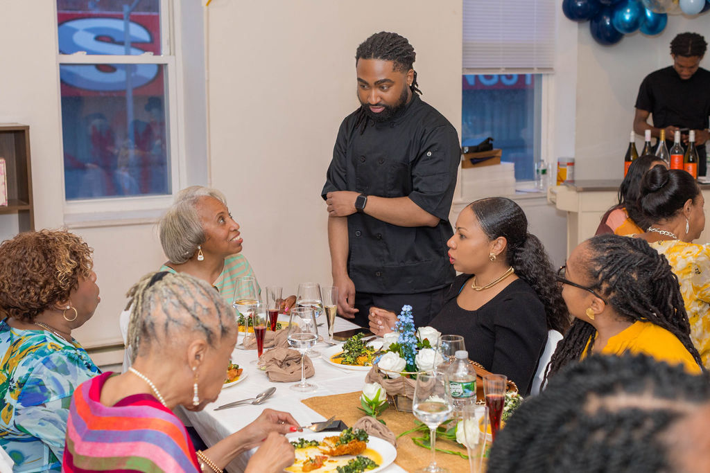 The head chef speaking with seated guests at the table during service — warmth and connection
