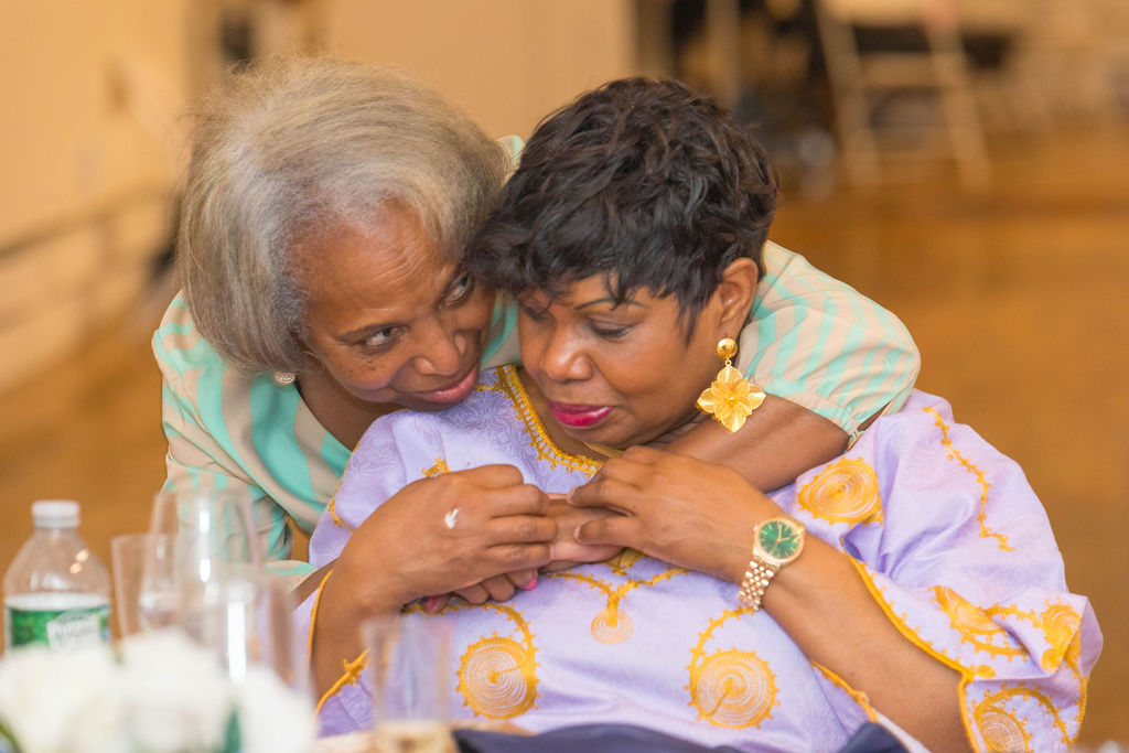 Two women in a quiet tender embrace — the emotional heart of the Mother's Day luncheon